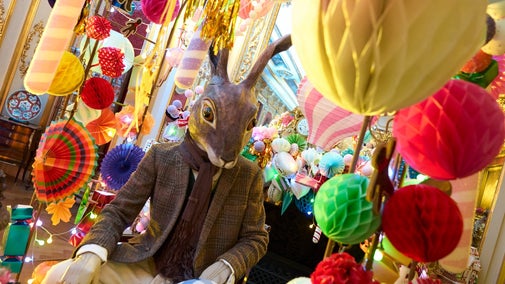 Alice's Christmas in Wonderland at Polesden Lacey 2025: a large, human-sized hare mannequin, dressed in a brown jacket and scarf, sits at a tea table with brightly coloured Christmas decorations behind him